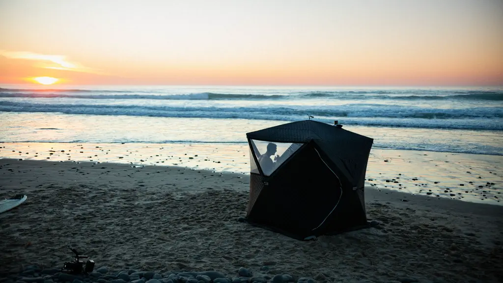 Person relaxing inside Overland Sauna tent on the beach at sunset